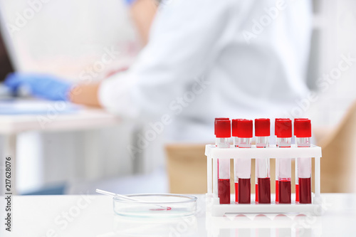 Test tubes with blood samples and scientist working on computer in laboratory