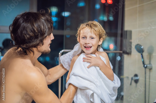 Dad wipes his son with a towel after a shower in the evening before going to sleep on the background of a window with a panoramic view of the city photo