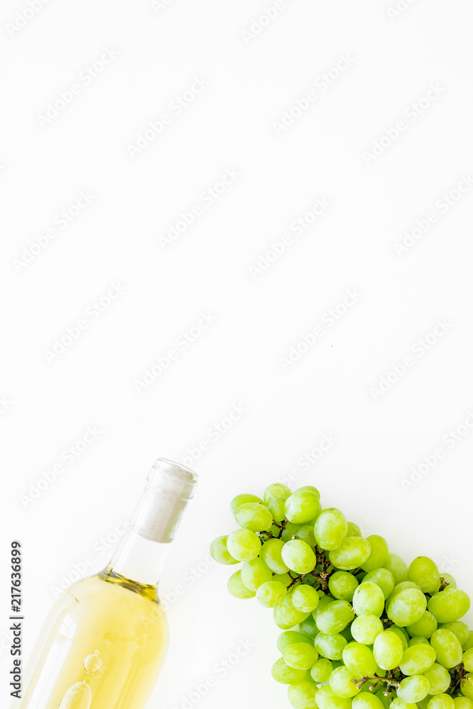 White wine in glass bottle near bunch of grapes on white background top view copy space White wine in glass bottle near bunch of grapes on white background top view copy space