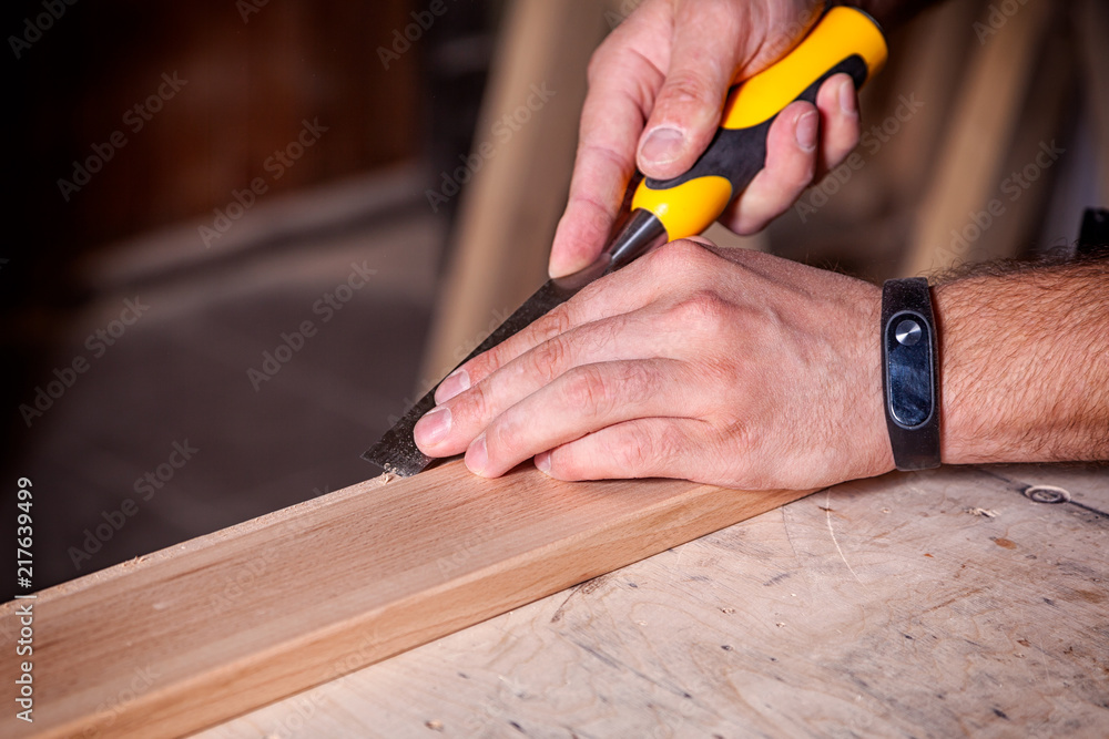 Close up of a young man builder treating a wooden product with a chisel in the workshop Close up of a young man builder treating a wooden product with a chisel in the workshop