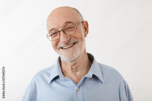 Happy emotional sixty year old man with bald head, gray stubble and wrinkled face having joyful cheerful look, smiling broadly at camera, showing healthy straight teeth. Human feeling and reaction