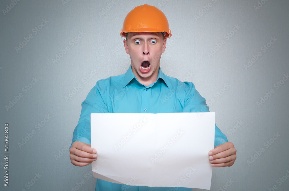 Shocked builder construction worker is holding in hand a plan draft document isolated on gray background. Shocked builder construction worker is holding in hand a plan draft document isolated on gray background.