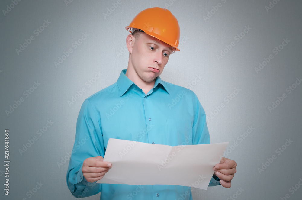 Perplexed builder construction worker is holding in hand a plan draft document isolated on gray background. Perplexed builder construction worker is holding in hand a plan draft document isolated on gray background.
