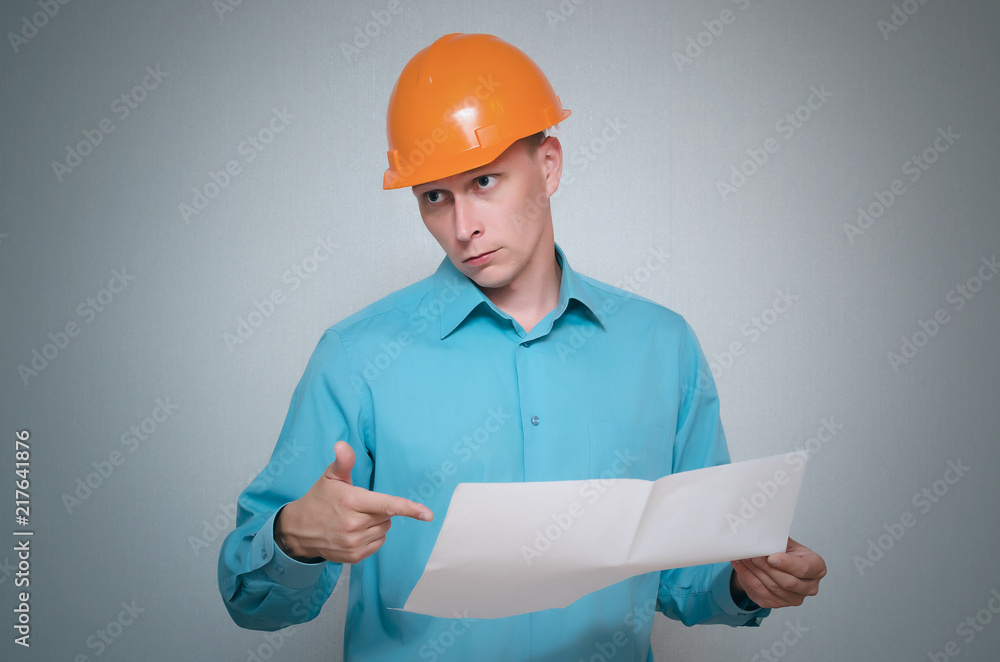 Confused builder construction worker is holding in hand a plan draft document isolated on gray background. Confused builder construction worker is holding in hand a plan draft document isolated on gray background.