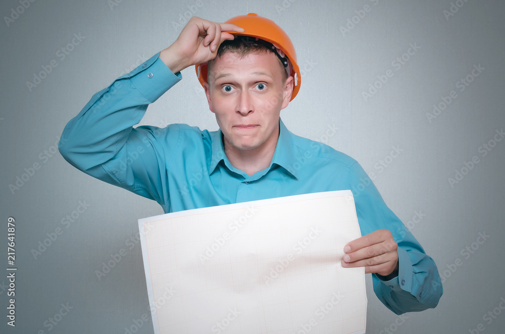 Confused builder construction worker is holding in hand a plan draft document isolated on gray background. Confused builder construction worker is holding in hand a plan draft document isolated on gray background.