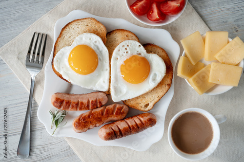 Breakfast with love - fried eggs in the shape of a heart, fried sausages and coffee