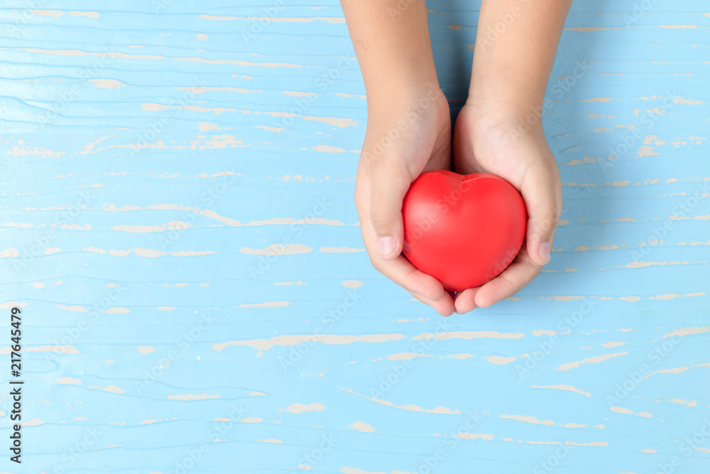 Fototapeta premium child hands holding red heart on blue wood