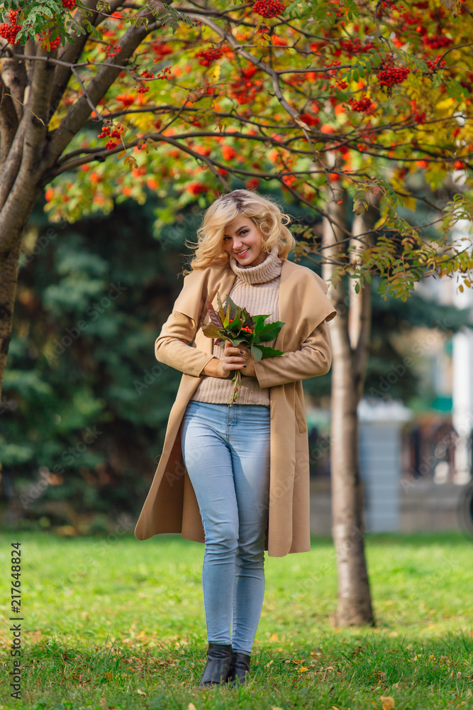 Beautiful elegant woman standing under the rowan tree in autumn park
