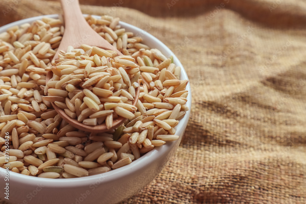 Raw brown rice in a spoon and bowl. top view food background