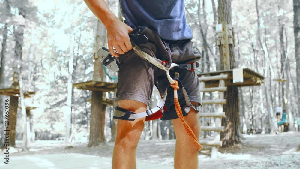 Person puts on safety climbing equipment 4K. Low angle tilt up of safety equipment in focus with a desaturated climbing park in the background out of focus. Creative image. Person puts on safety climbing equipment 4K. Low angle tilt up of safety equipment in focus with a desaturated climbing park in the background out of focus. Creative image.