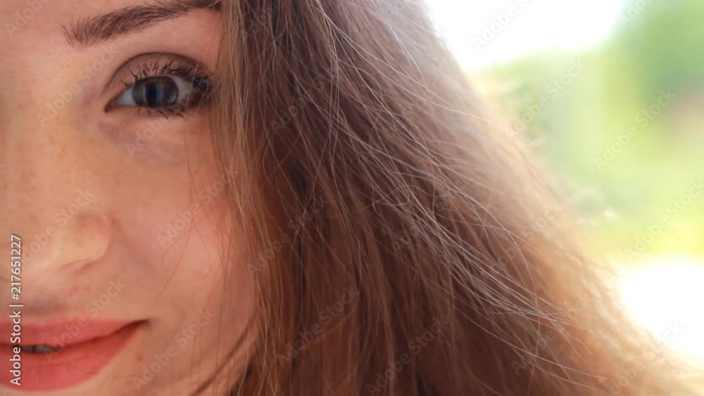 Portrait half face closeup young woman with brown hair smiling and winks on a windy day.