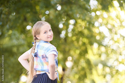 Little girl in green sunny forest along. Fun schoolgirl outside. Selective focus
