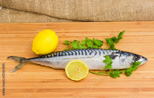 Uncooked Atlantic mackerel with lemons and parsley on cutting board