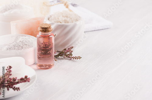 Gentle pink cosmetics oil, small flowers and white soap, cream, clay, towel closeup on white wooden background, copy space.