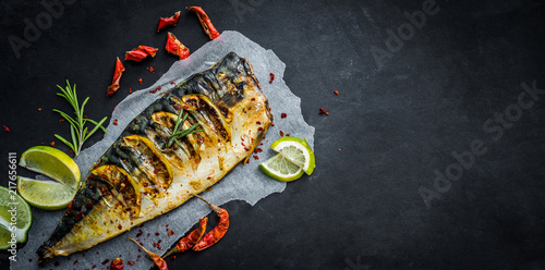Grilled mackerel fish with lime on a black background, copy space fried fish and vegetables