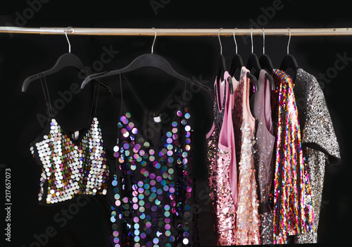 Row of vest with sequins colorful sundress hanging on hanger– black background, 