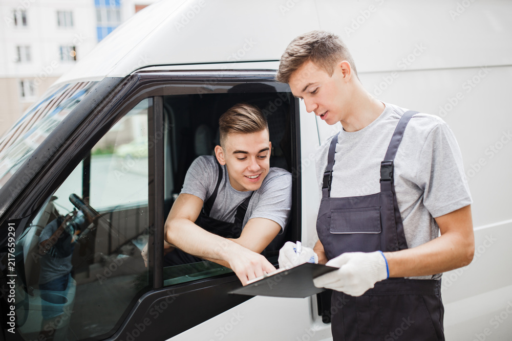 A young handsome guy wearing uniform is pointing at the clipboard. Another worker wearing uniform is looking at the clipboard. House move, mover service. A young handsome guy wearing uniform is pointing at the clipboard. Another worker wearing uniform is looking at the clipboard. House move, mover service.