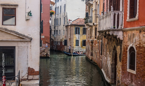 Beautiful old venetian narrow street with old shabby colorful buildings. Gondolier with paddle in his hands rides a gondola with tourists.