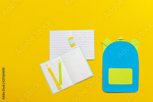 School bag backpack, notebooks and pencils paper cut on yellow background