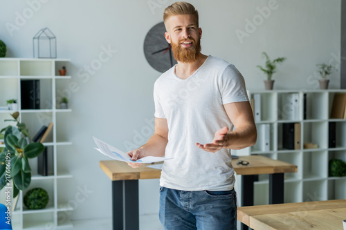 Bearded young businessman working at modern office.Man wearing white t-shirt and making notes on the documents.