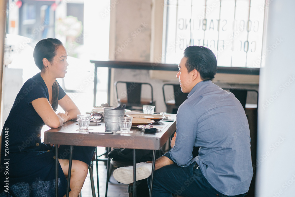 A couple having a meal in an indoor restaurant during their date. They are having a conversation while waiting for their food to arrive. A couple having a meal in an indoor restaurant during their date. They are having a conversation while waiting for their food to arrive.