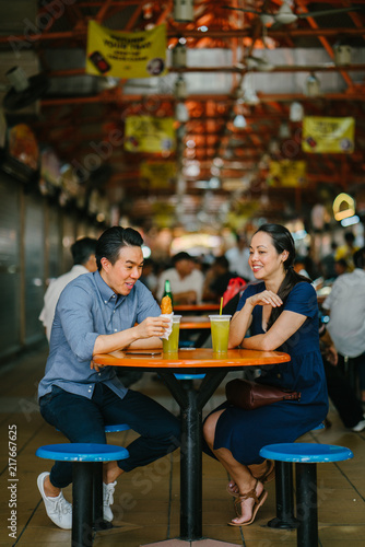An image of a young Chinese Asian couple at a hawker center in Singapore, Asia. They are enjoying their snacks on a beautiful weekend.