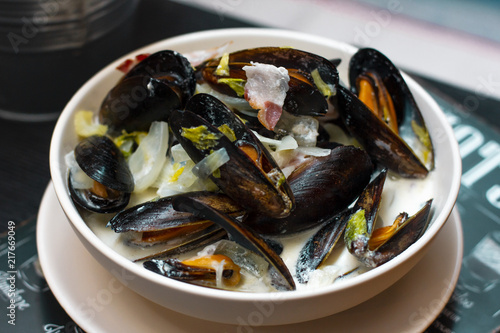 Mussels with onions and bacon in cream sauce in deep plate on the table