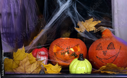 Halloween pumpkin in the mystical house window with rain drope and spider web, a ghost face in the background photo