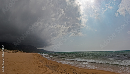 Golden sand dunes on the beach of Portixeddu in Sardinia, high above a sky full of black and threatening clouds. photo