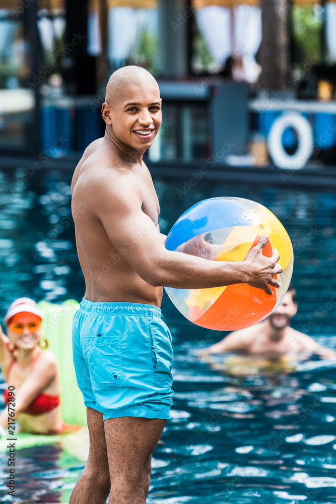 young muscular man with swimming ball looking at camera while his friends