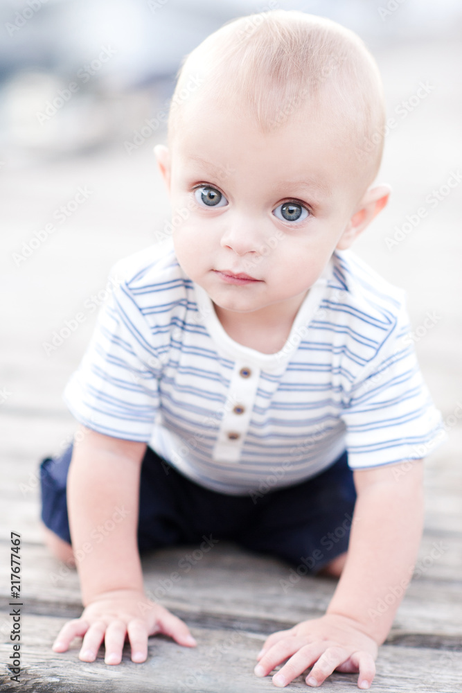 Cute baby boy crawling on wooden pier outdoors. Wearing striped clothes. Childhood. Cute baby boy crawling on wooden pier outdoors. Wearing striped clothes. Childhood.