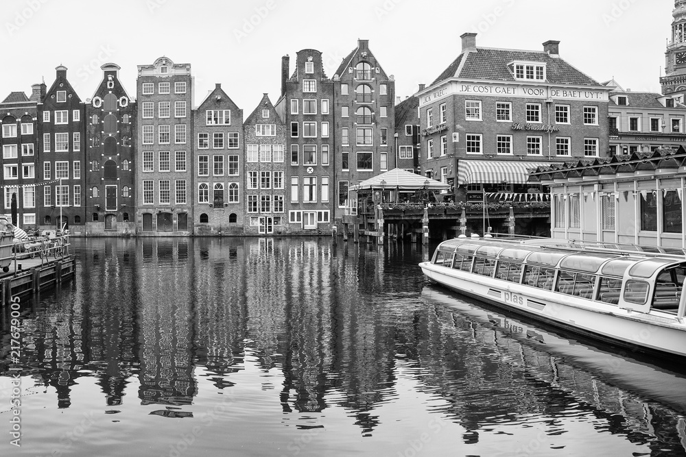 Fototapeta premium Charakterystyczne budynki Amsterdamu odbijające się w wodzie kanału, czarno-białe