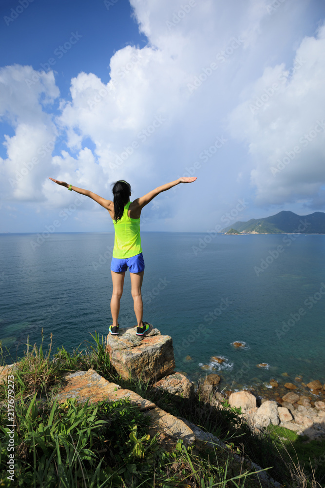 Woman enjoying nature with her opened arms on seaside cliff edge