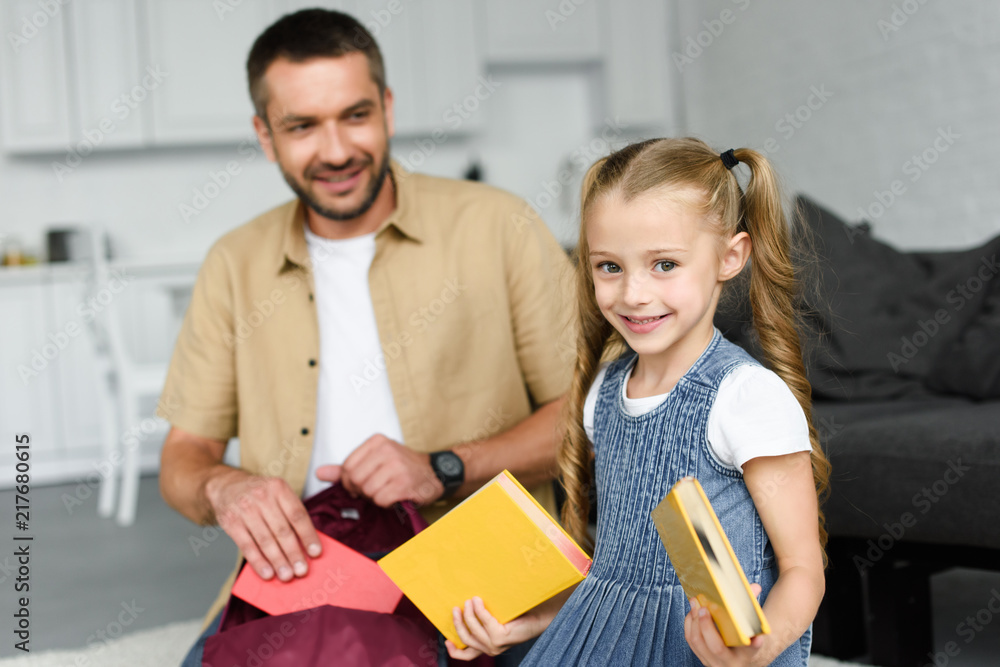 selective focus of smiling father helping little daughter packing backpack for first day at school, back to school concept selective focus of smiling father helping little daughter packing backpack for first day at school, back to school concept