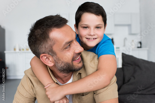 portrait of smiling boy hugging father and looking at camera at home