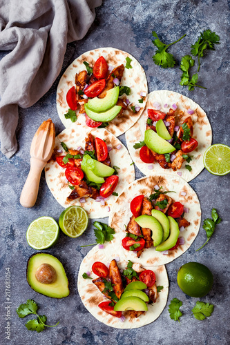 Mexican grilled chicken tacos with avocado, tomato, onion on rustic stone table. Recipe for Cinco de Mayo party. Top view, overhead, flat lay.