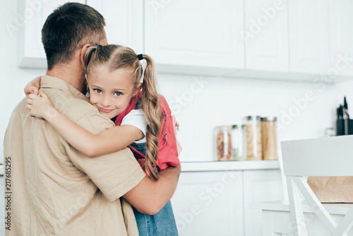 father and little daughter with backpack hugging each other in kitchen at home  back to school concept