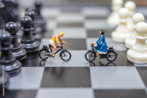 Miniature women and man on bicycle opposite site with chess on back as a business negotiation or business agreement.