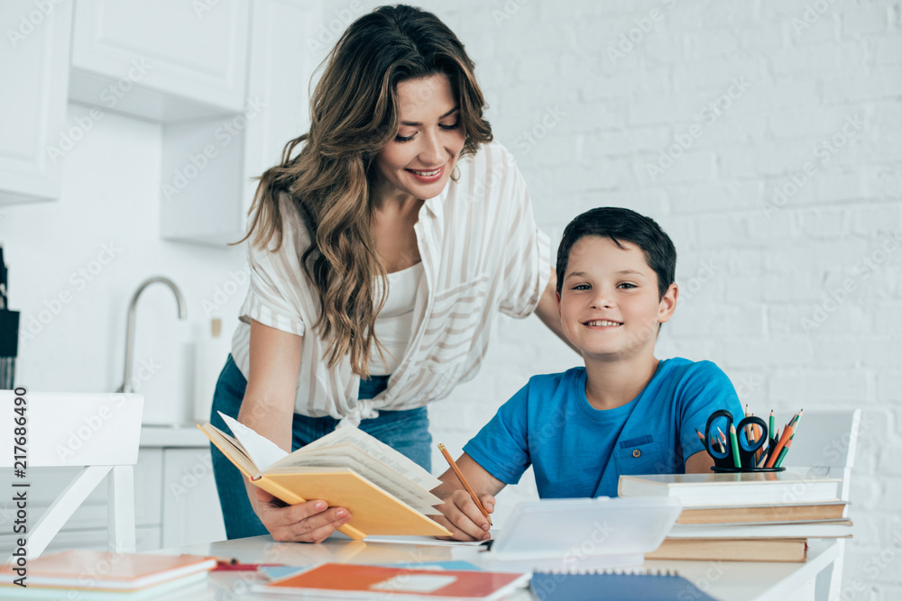 portrait of mother helping smiling son with homework in kitchen at home portrait of mother helping smiling son with homework in kitchen at home