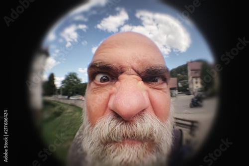 an angry man looking to a peephole door photo