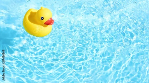 A yellow rubber duck can drift relaxed from top to bottom through the picture, on the sparkling and crystal-clear water of a pool in the summer light photo