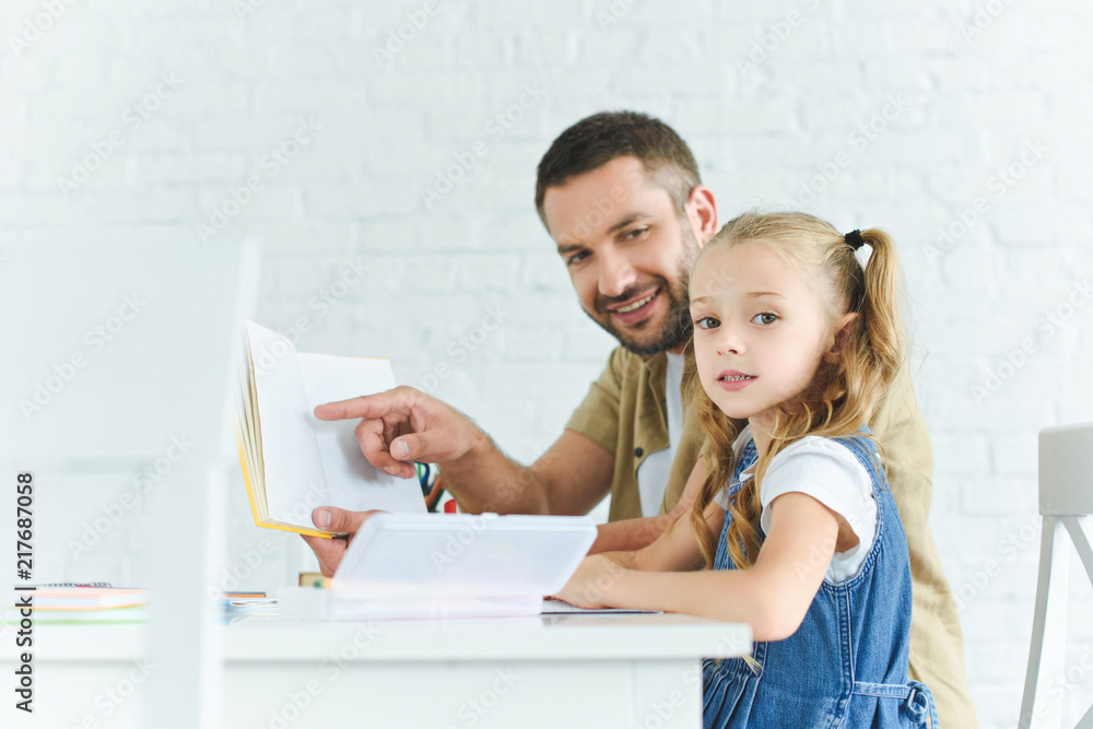 side view of smiling father and little daughter doing homework together at home side view of smiling father and little daughter doing homework together at home