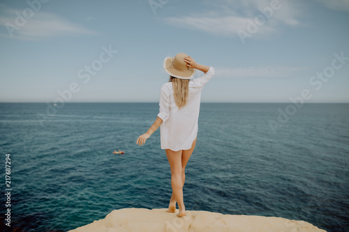 Girl in the white t-shirt is resting on the edge of a mountain on a background of a sea. Lifestyle traveler