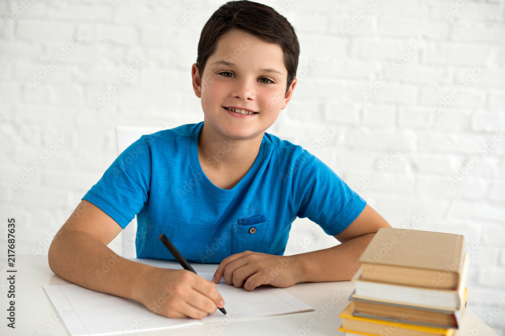 portrait of smiling boy doing homework alone at table at home portrait of smiling boy doing homework alone at table at home