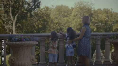 Rear view of milti ethnic family with two little mixed race girls admiring scenic view in travel location while leaning on stone railing during summer vacations. Happy diverse family on their vacation photo