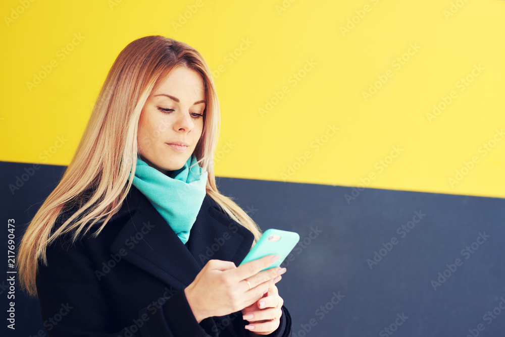 Beautiful young woman using an application to send an sms message in her smartphone device .Beautiful girl writes sms on phone. girl checking email box standing on publicity area Beautiful young woman using an application to send an sms message in her smartphone device .Beautiful girl writes sms on phone. girl checking email box standing on publicity area