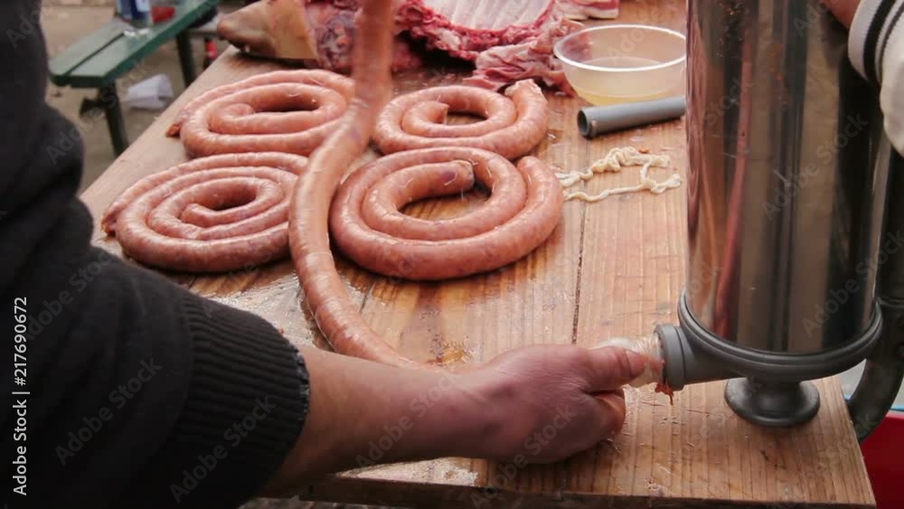 Butcher is stuffing pig intestine with minced meat to make sausages. Fill up pig intestines to