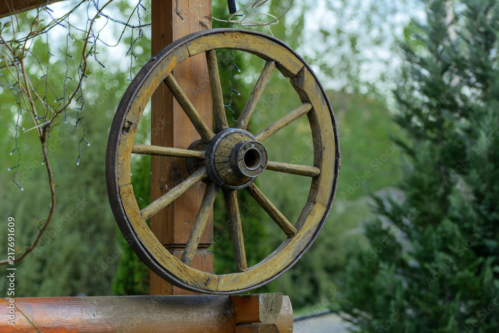Wheel of the past. An ancient old wooden wheel from a rural cart is nailed to a wooden pole against the sky and green vegetation.