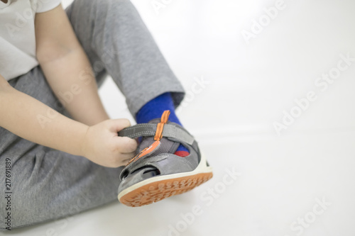 Small child tries to put on his shoes. Baby boy with shoes in hand isolated on white.