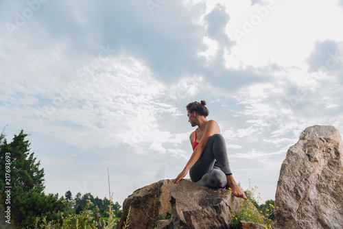 Sitting and stretching. Fit and healthy woman wearing red top sitting and stretching on rock